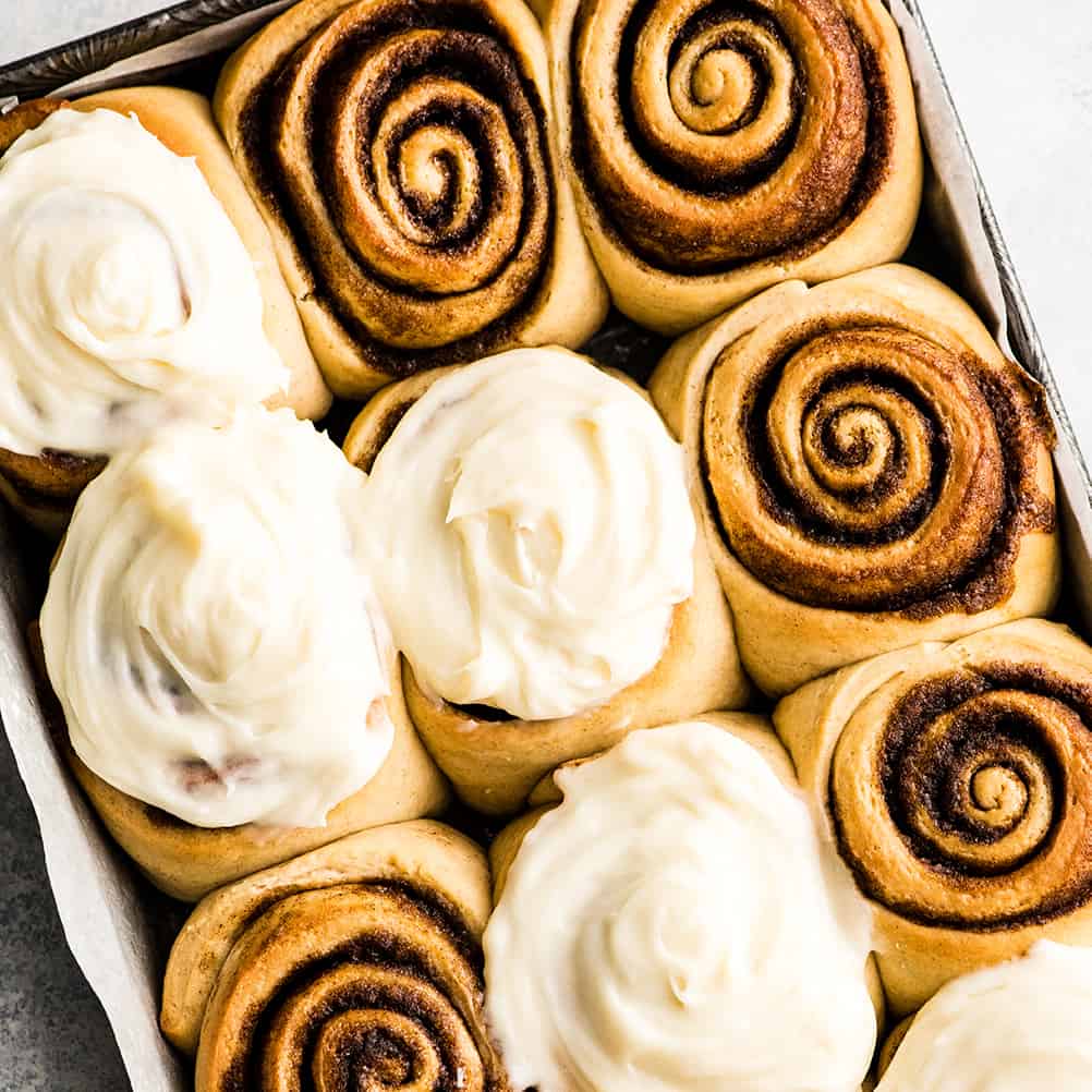 overhead photo of 12 cinnamon rolls in a baking pan, some frosted some unfrosted