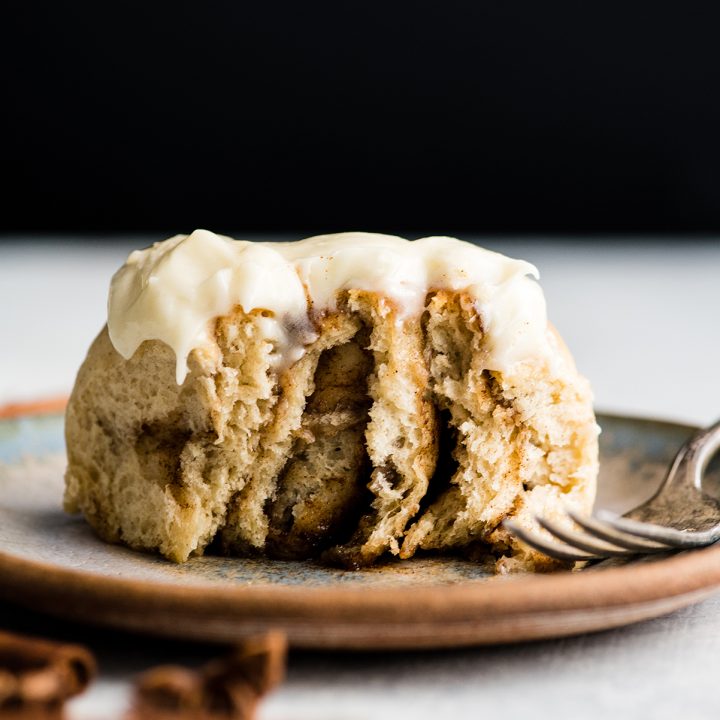 front photo of a cinnamon roll on a plate with a bite taken out