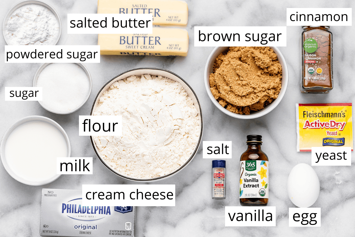 This is the Best Homemade Cinnamon Rolls Recipe EVER! These gooey cinnamon rolls are even better than Cinnabon cinnamon rolls, and are topped with a delicious cream cheese frosting! They're easy to make and can be prepared the day before and left to rise overnight in the refrigerator. overhead view of the ingredients in this cinnamon rolls recipe in bowls and labeled like whole milk, flour, yeast, butter, granulated sugar, vanilla, sea salt, cinnamon, eggs and brown sugar.