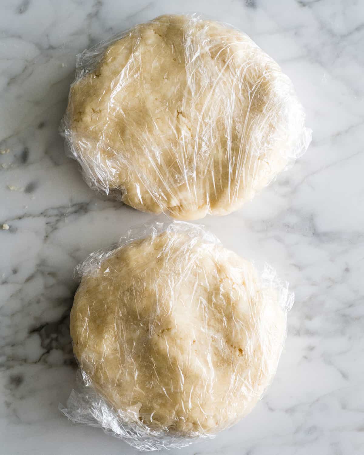 two discs of How to butter Pie Crust wrapped in plastic wrap to chill