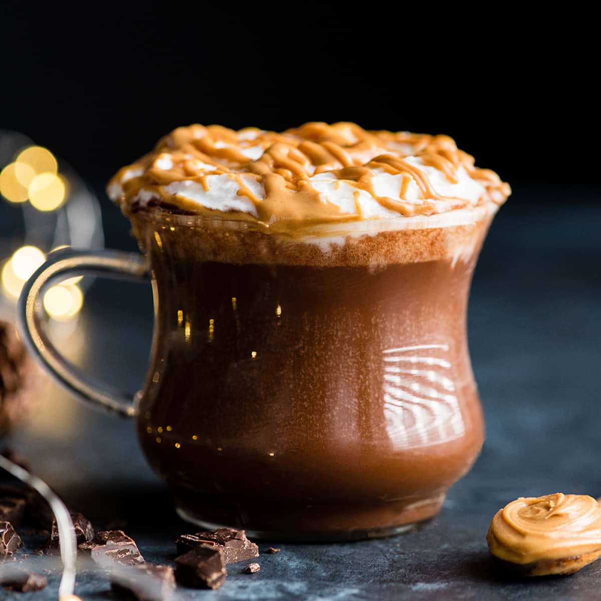 peanut butter hot chocolate in a glass mug topped with whipped cream & peanut butter drizzle