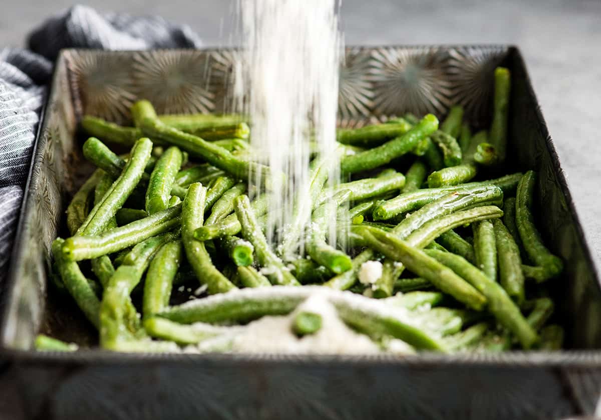 front view of parmesan cheese being poured onto green beans in a baking sheet in the making of this Roasted Parmesan Green Beans recipe