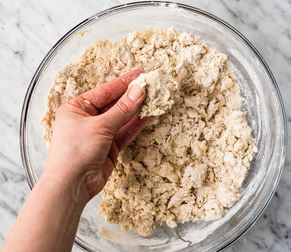 overhead view o fa bowl of Cinnamon Scone dough after it has been mixed. A hand is over the bowl showing a piece of the dough being pinched together. 