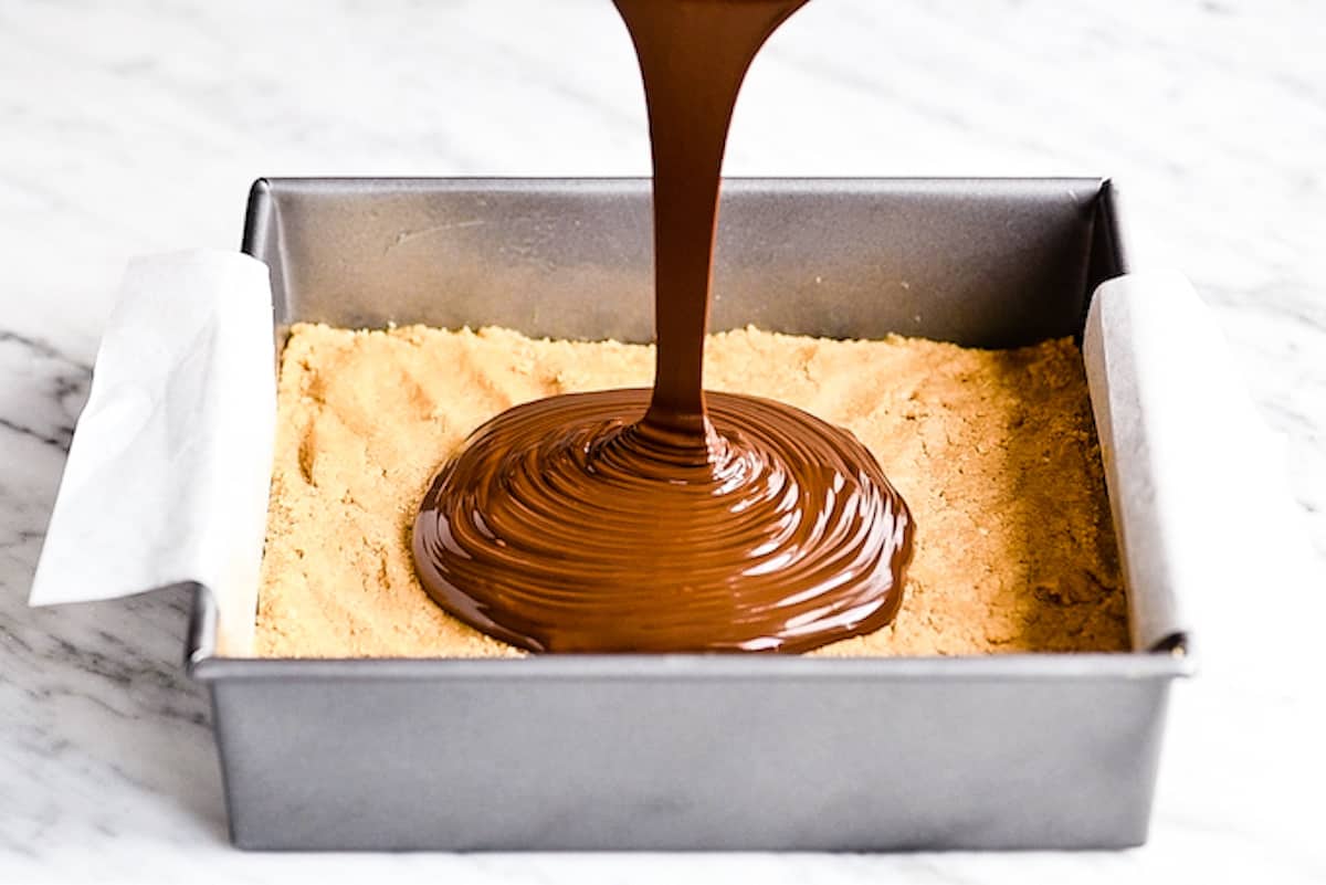 front view of the melted chocolate peanut butter mixture being poured on top of the pan with the peanut butter base layer in the making of these No-Bake Chocolate Peanut Butter Bars