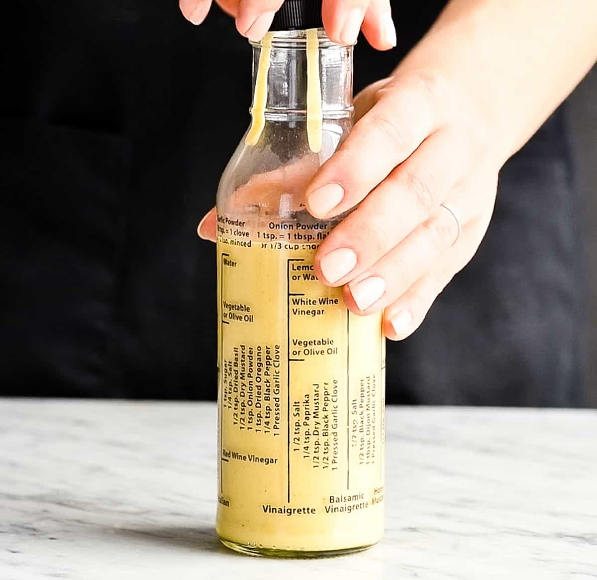 Front view of a hand putting the lid on a bottle of homemade Apple Cider Vinaigrette dressing