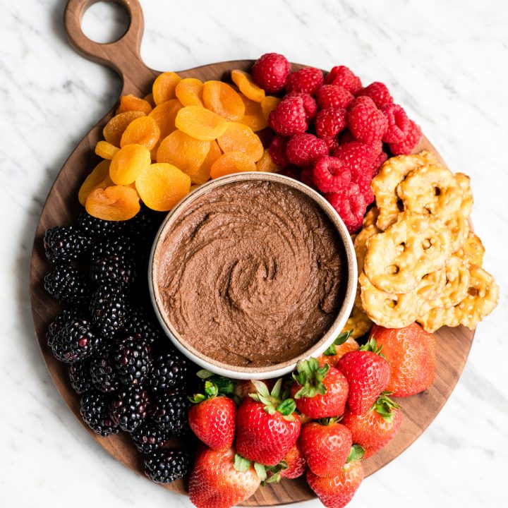 Overhead view of Chocolate Hummus in a bowl surrounded by fruits and pretzels to dip in it