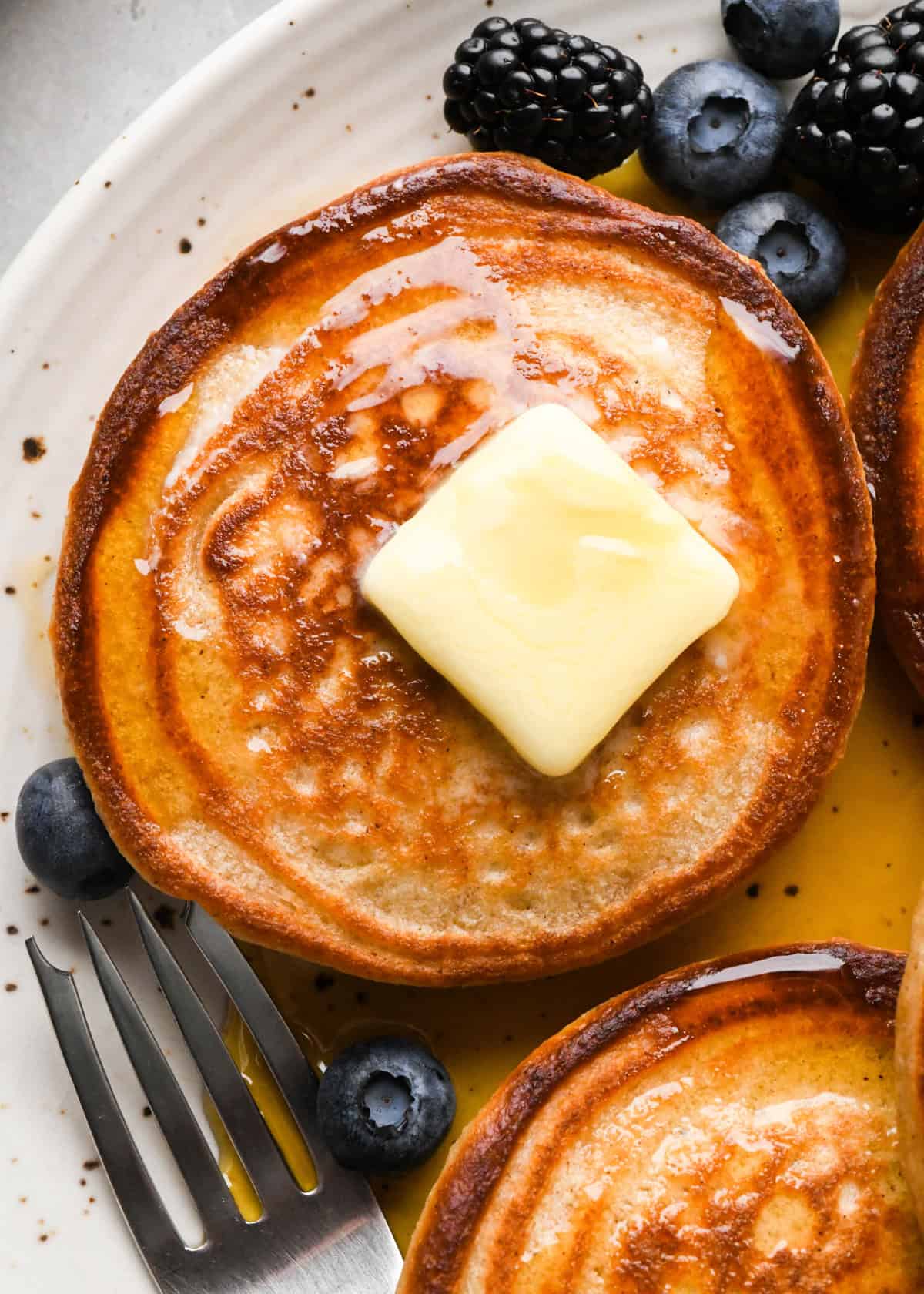 3 greek yogurt pancakes on a white ceramic plate with butter, syrup and berries 