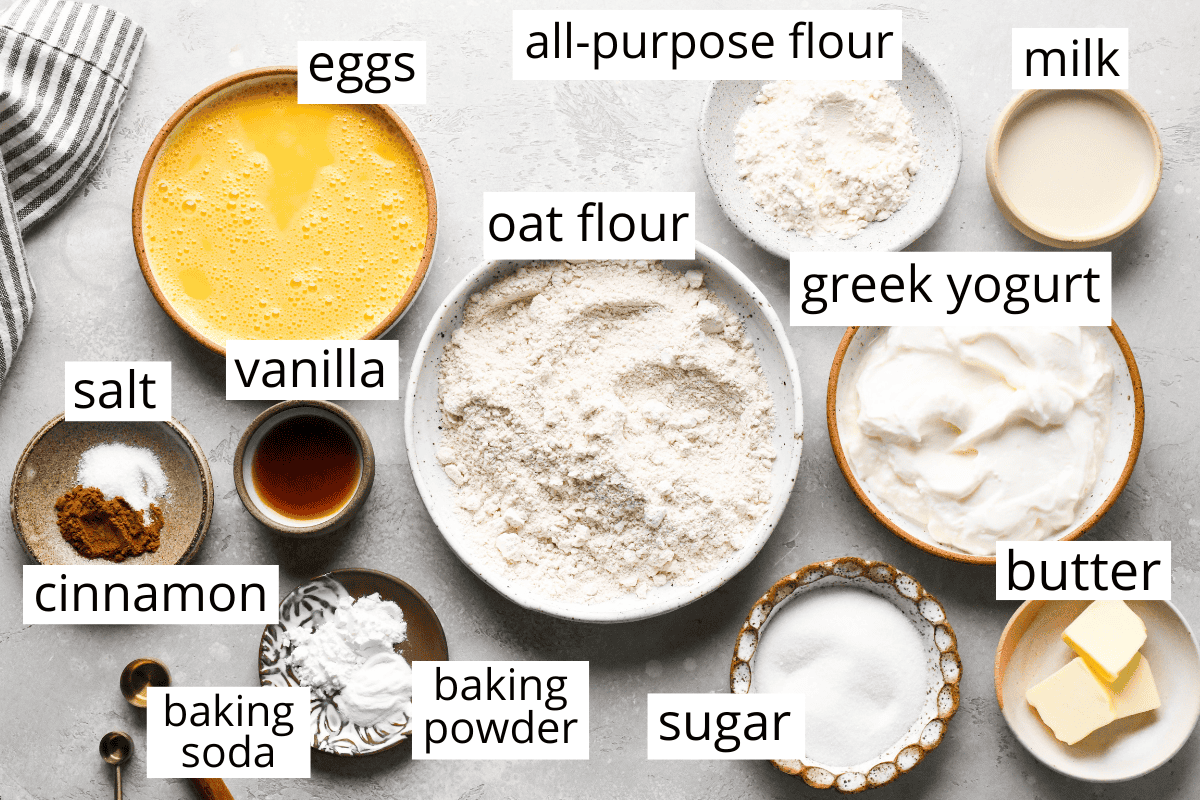 overhead photo of the ingredients for this greek yogurt pancakes recipe all in bowls and labeled. Ingredients include greek yogurt, eggs, oat flour, sugar, butter milk and flour. 