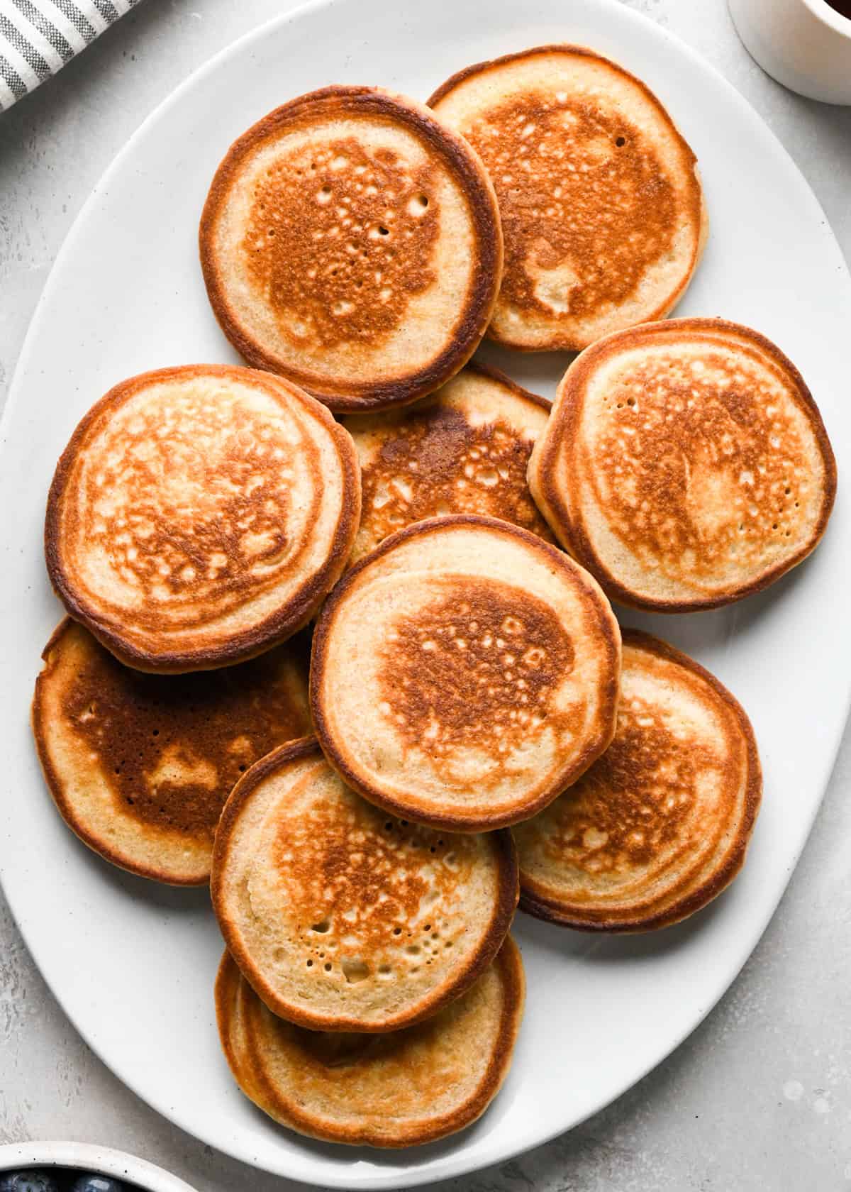 9 greek yogurt pancakes on a white, oval serving plate. 