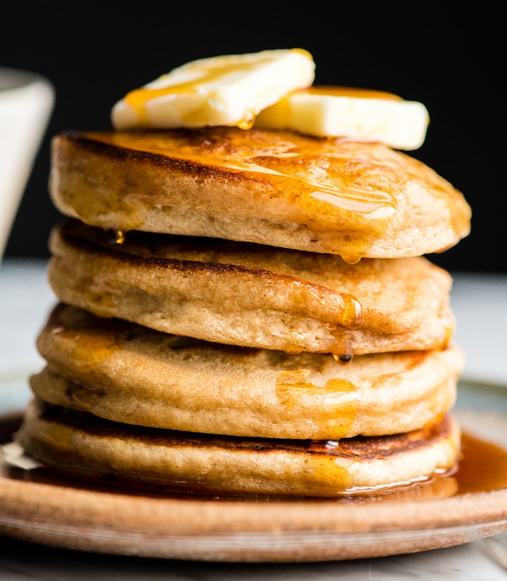 Front view of a stack of four Greek Yogurt Pancakes with butter on top and maple syrup