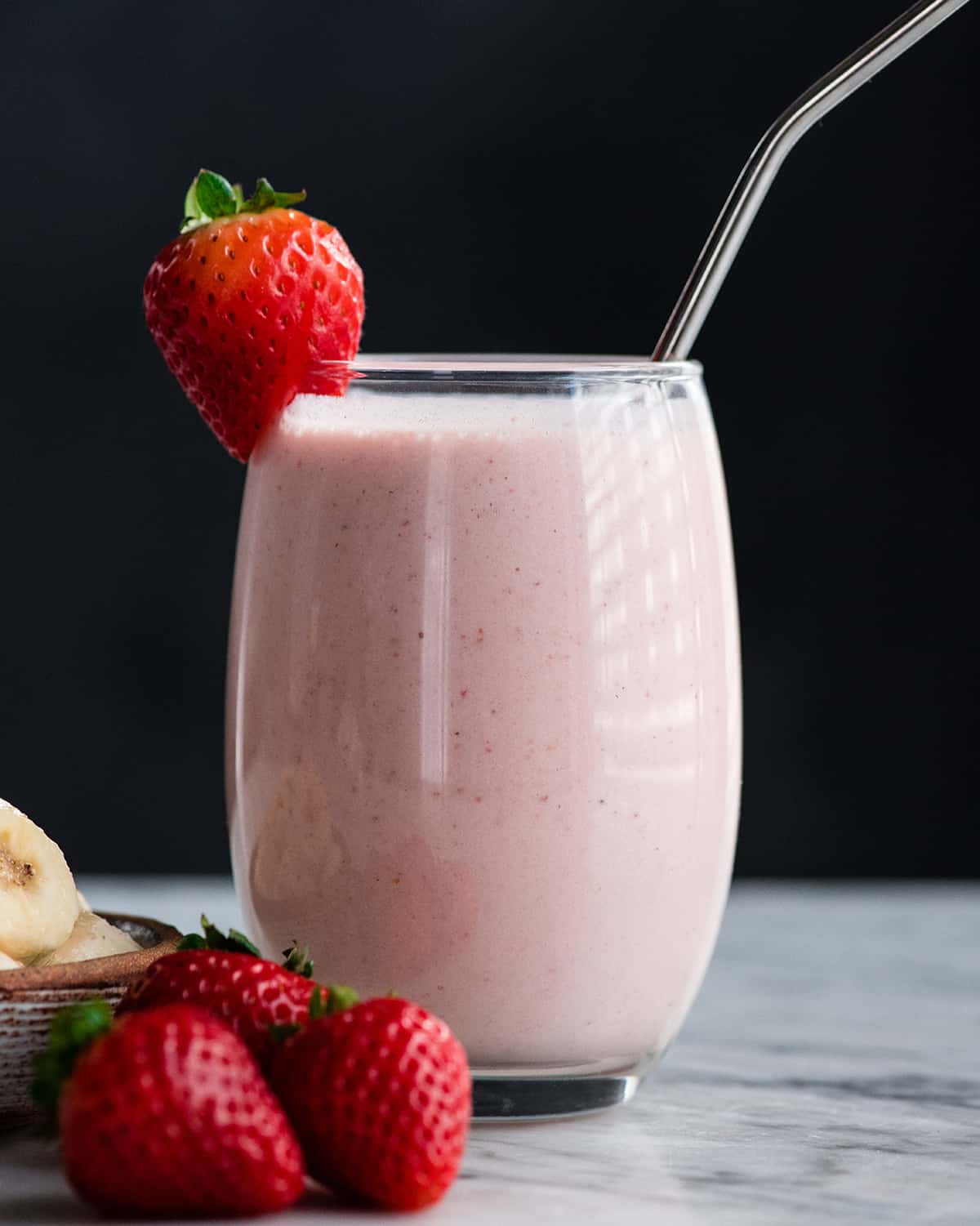 a glass filled with strawberry banana smoothie with a straw and strawberries.