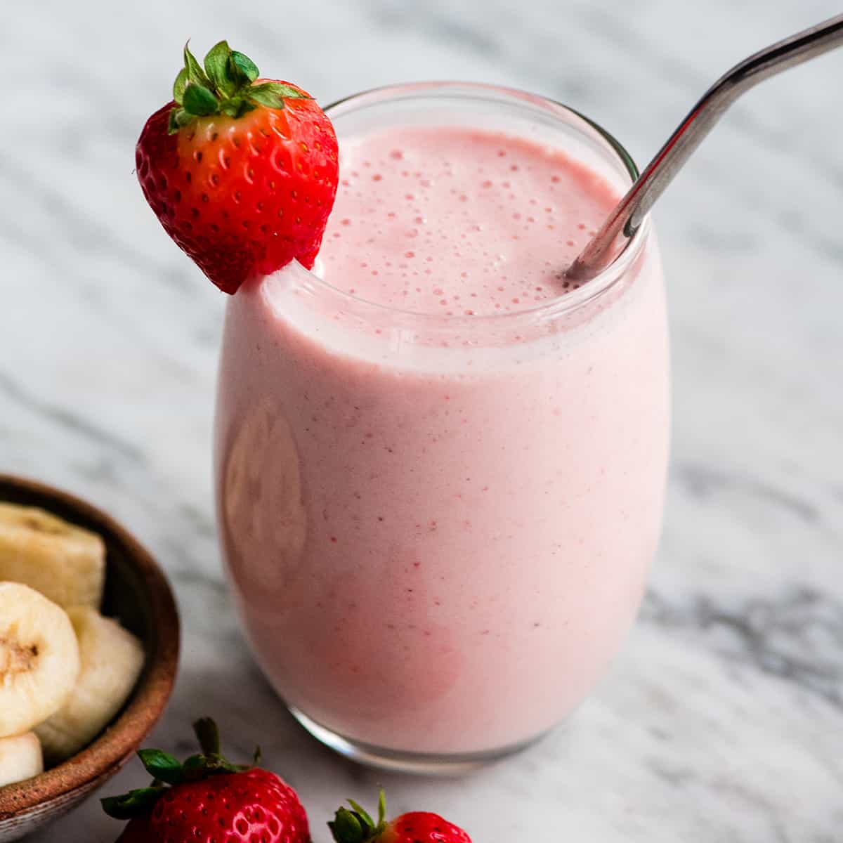  a glass filled with strawberry banana smoothie with a straw and strawberries.