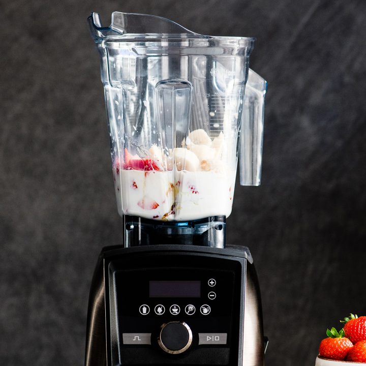 Front view of a Vitamix blender with the ingredients in it to make a Strawberry Banana Smoothie before blending