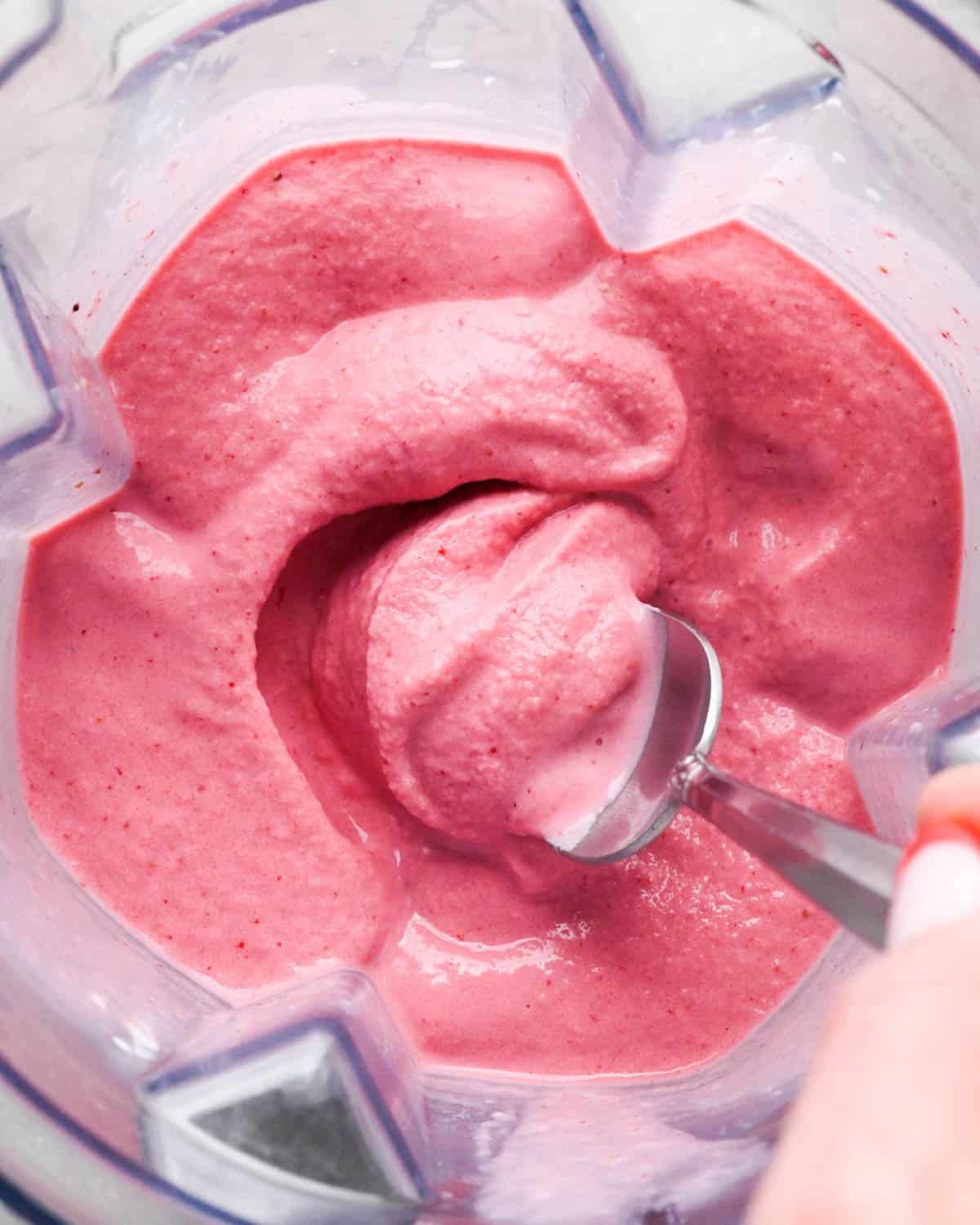 a spoon scooping thick and creamy strawberry banana smoothie in a blending container.