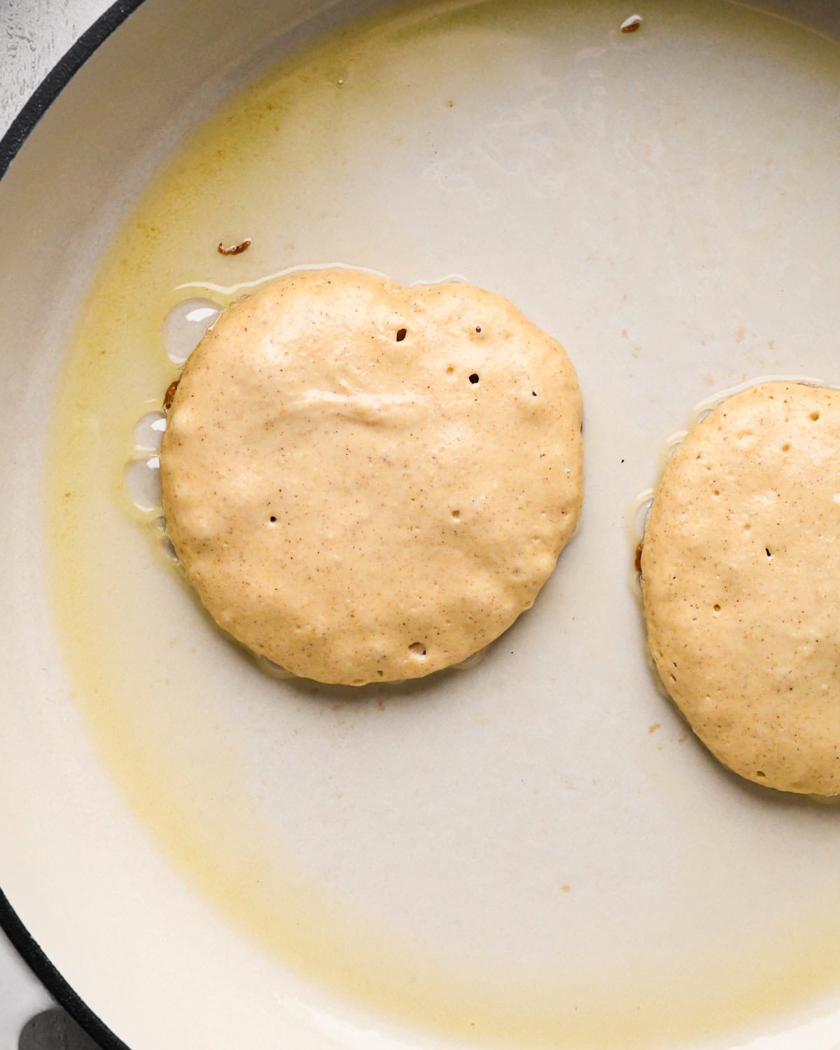 two greek yogurt pancakes after cooking until the batter starts bubbling in a white buttered skillet