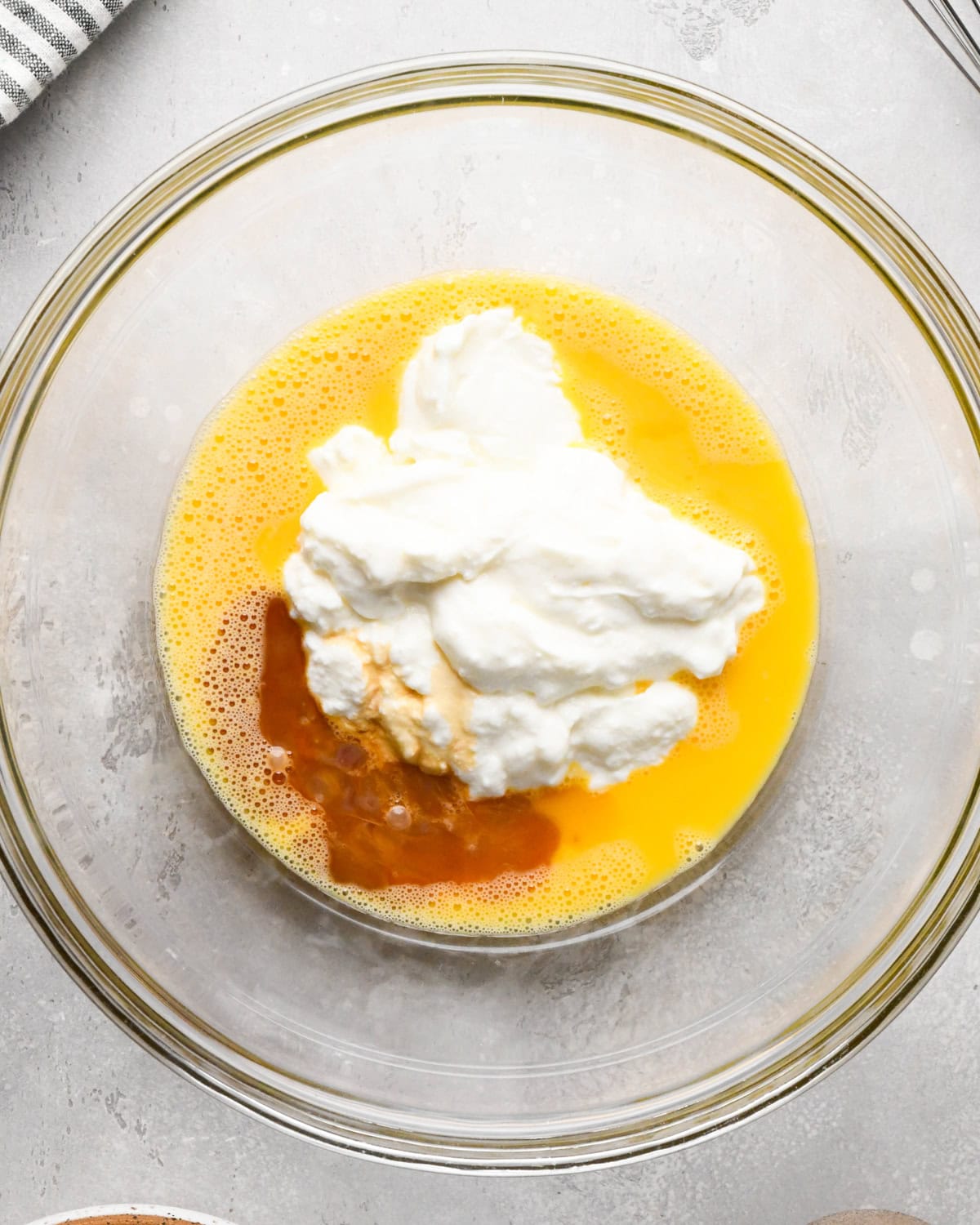 greek yogurt, eggs and vanilla in a glass mixing bowl on a gray surface before mixing making greek yogurt pancakes