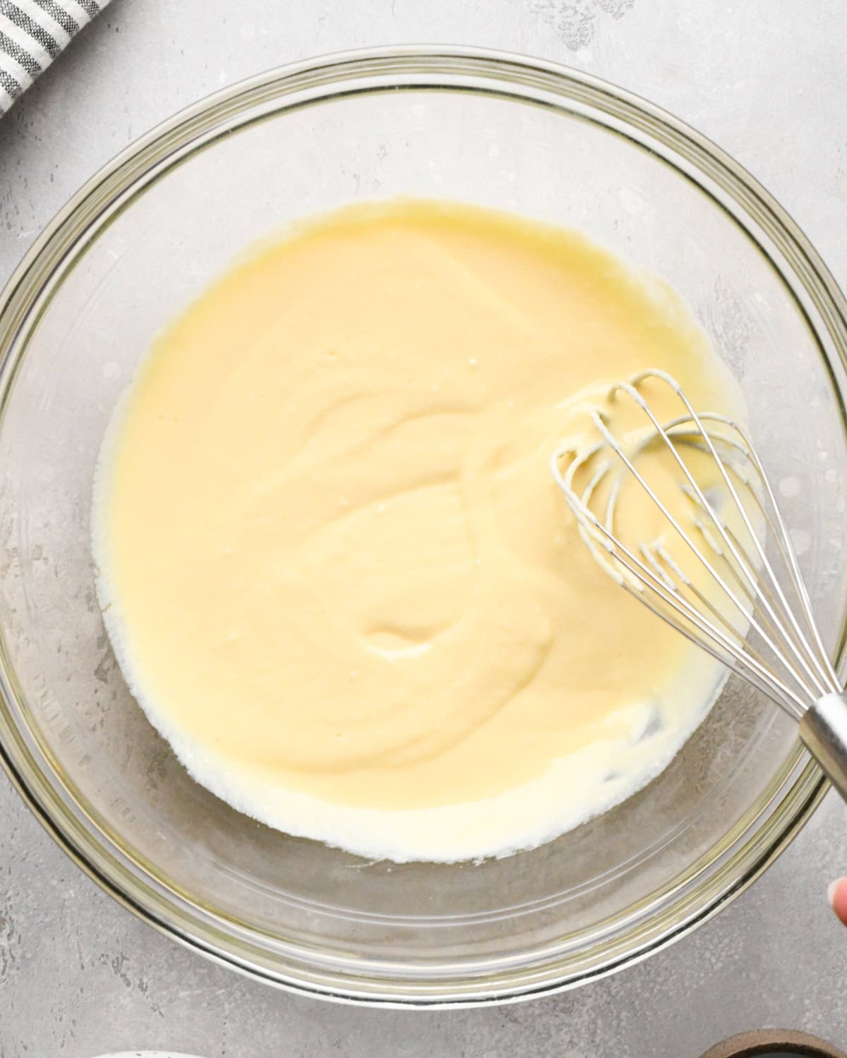 greek yogurt, eggs, and vanilla after being whisked together in a glass bowl on a gray surface with a wire whisk in the bowl making greek yogurt pancakes