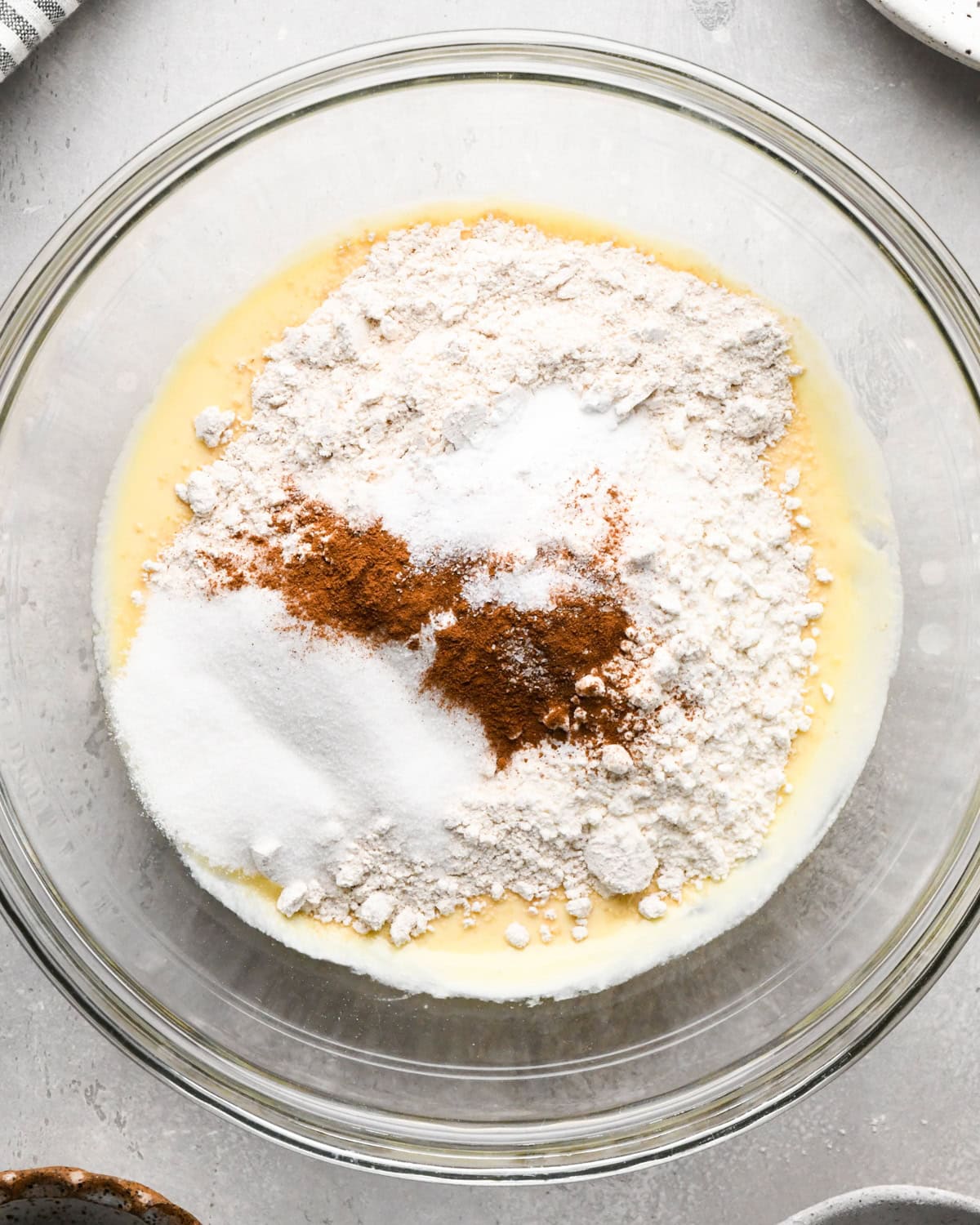 flour, salt, baking soda, baking powder, sugar and cinnamon added to the wet ingredients before mixing in a glass bowl on a gray surface making greek yogurt pancakes