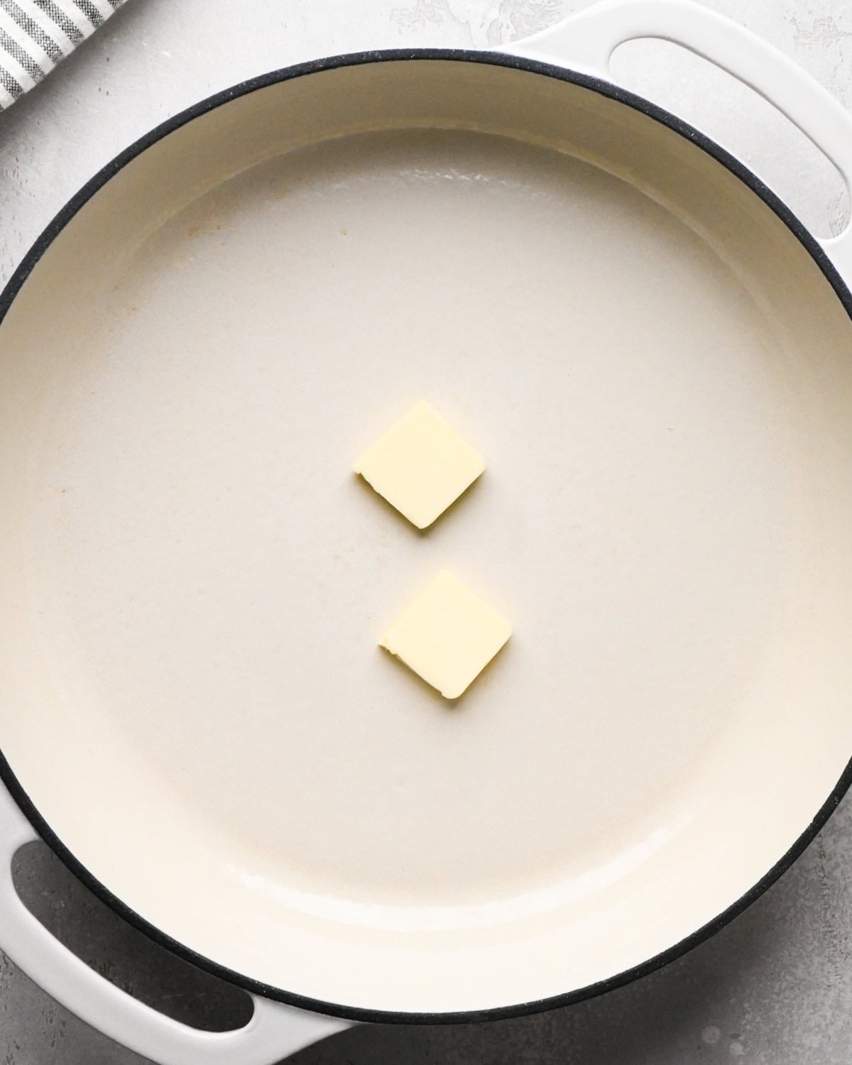 two square pieces of butter in a white skillet before melting, making greek yogurt pancakes