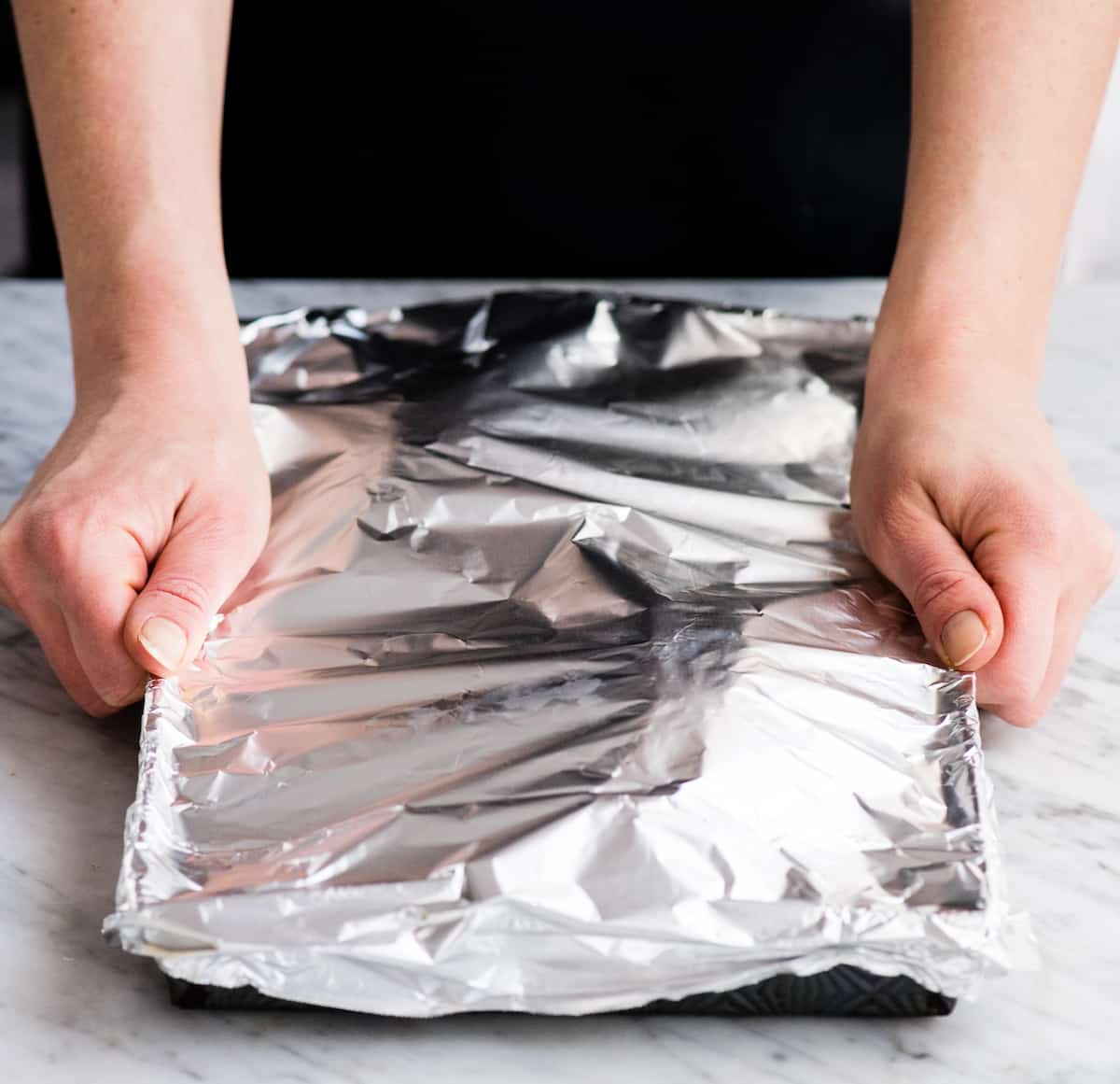 front view of hands placing aluminum foil over a baking sheet before placing it in the oven to make Spaghetti Squash Mac and Cheese