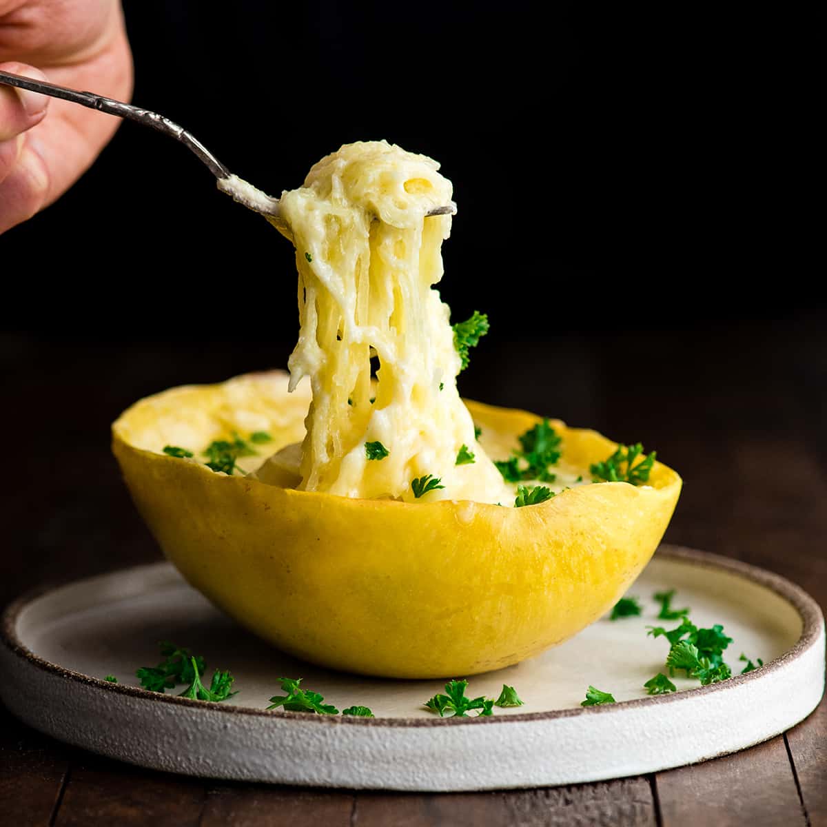 Front view of a hand holding a fork pulling a bite of Spaghetti Squash Mac and Cheese out of the shell