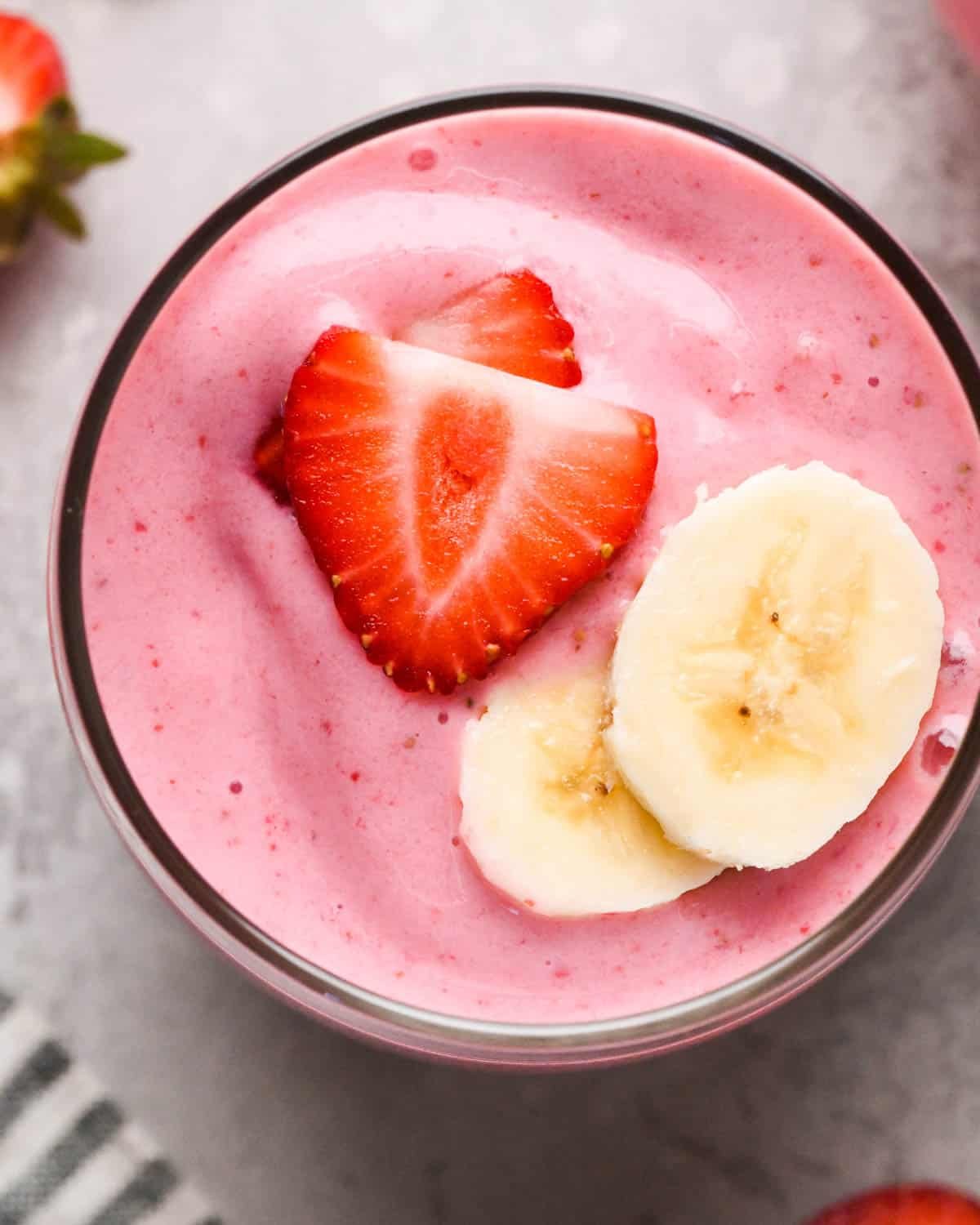 up close overhead photo of strawberry banana smoothie in a glass topped with two sliced strawberries and two sliced bananas surrounded by strawberries.