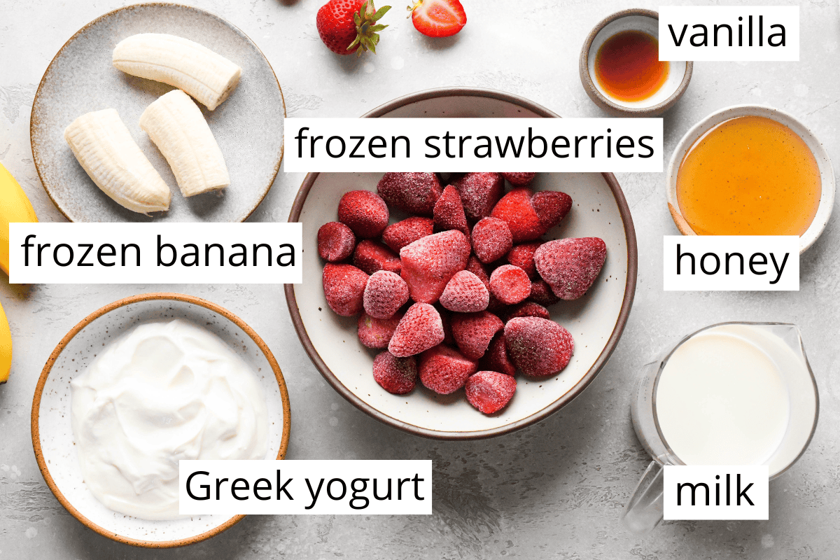The BEST strawberry banana smoothie recipe ever! It's easy (ready in less than 5 minutes), healthy, and made with yogurt so it's full of protein! It's the perfect snack or breakfast! #smoothie #strawberrybananasmoothie #strawberry #banana #breakfast #snack #vitamix overhead photo of the labeled ingredients in this strawberry banana smoothie recipe all in bowls - frozen strawberries, frozen bananas, greek yogurt, milk, vanilla, and honey