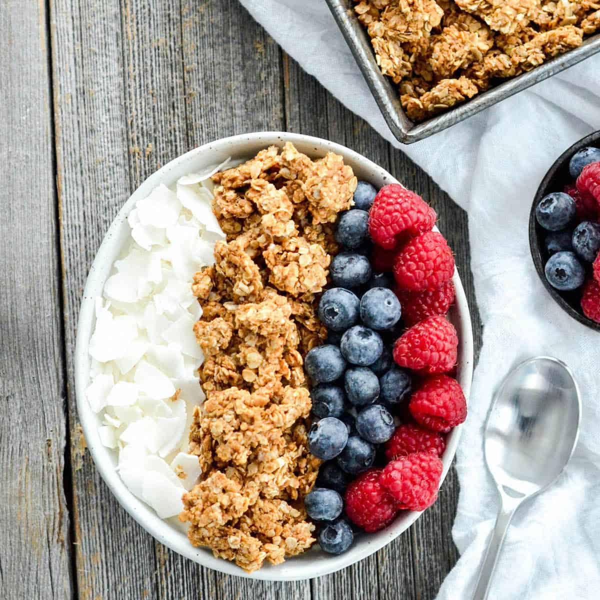 overhead view of peanut butter granola in a bowl with berries and coconut