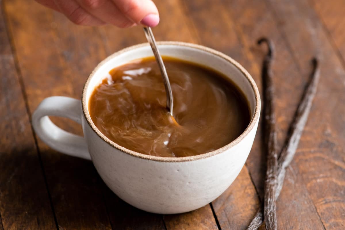 overhead view of a hand holding a spoon stirring the healthy coffee creamer into a mug of coffee