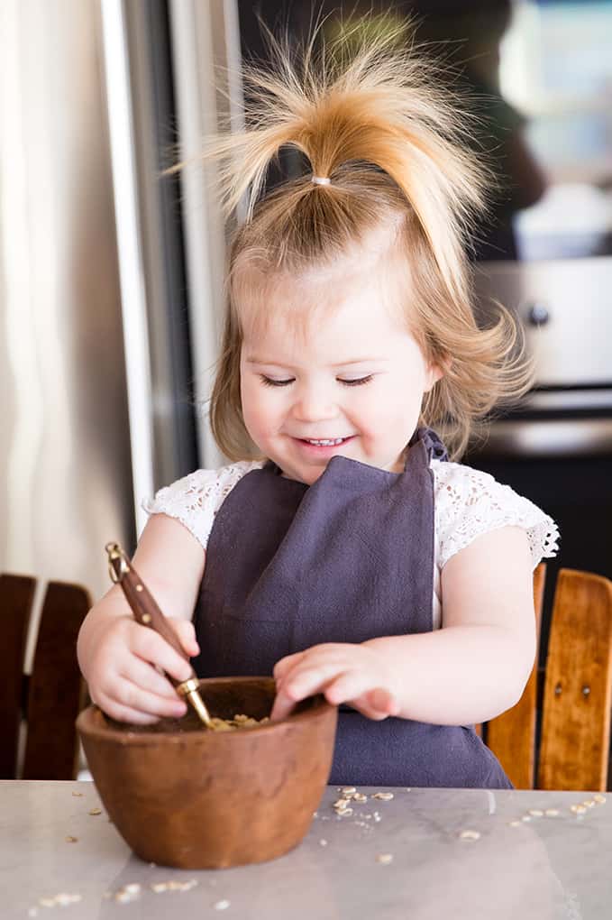 front view of a little girl playing with a measuring spoon and bowl while her mom is Front view of a mom and her four kids blending in a blender while she's Cooking with Kids