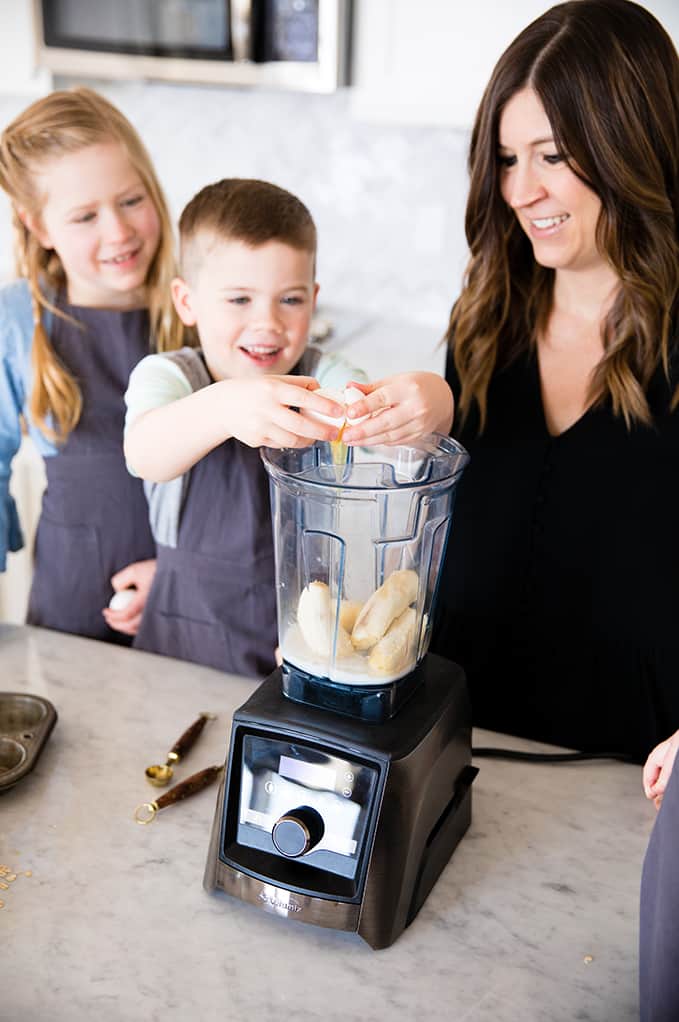 front view of a boy cracking an egg into a blender while his mom and sister watch in this article about Front view of a mom and her four kids blending in a blender while she's Cooking with Kids