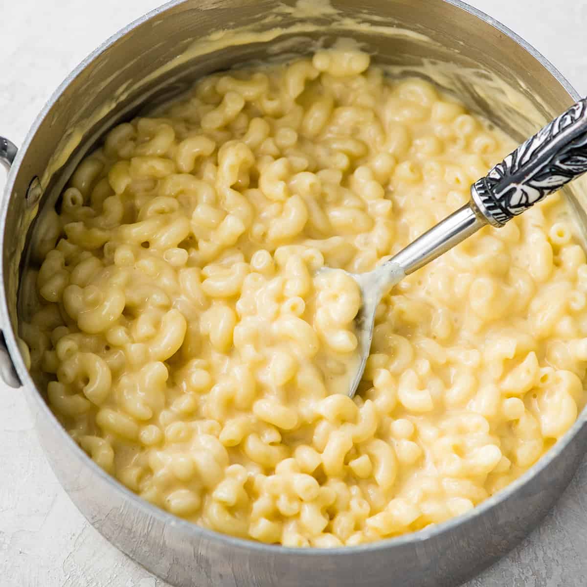 a spoon taking a scoop of homemade mac and cheese out of a saucepan
