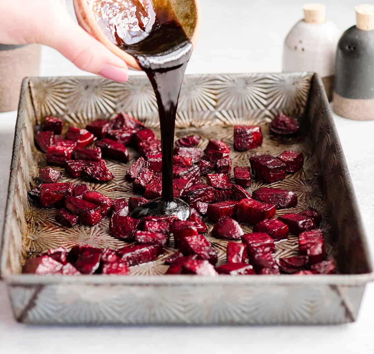 photo showing How to Roast Beets pouring balsamic vinegar on the partially roasted beets in a pan