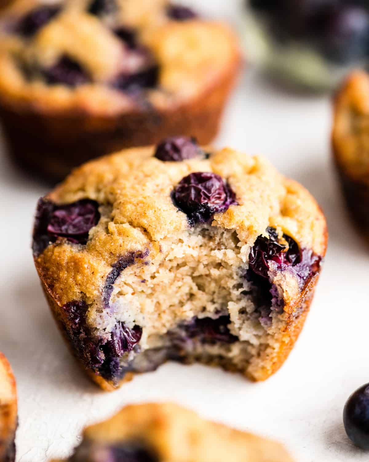 a paleo blueberry muffin with a bite taken out of it surrounded by other muffins & berries