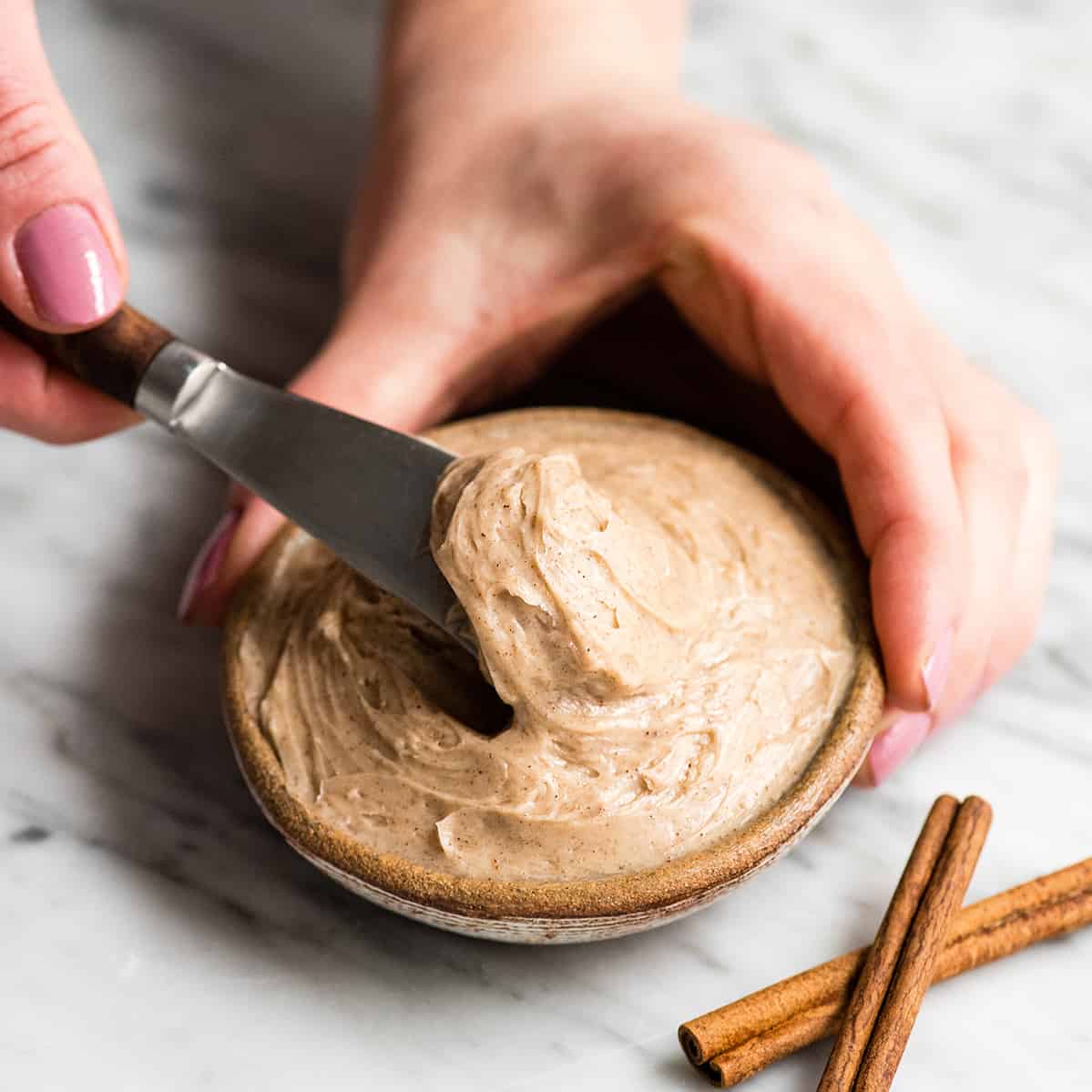 front view of a hand using a knife to scoop some Cinnamon Honey Butter out of a small dish