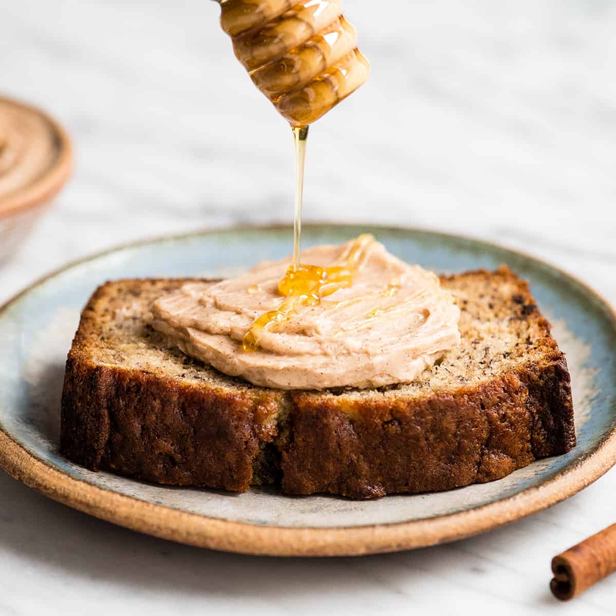 front view of honey being drizzled on Cinnamon Honey Butter on a piece of banana bread on a plate. 
