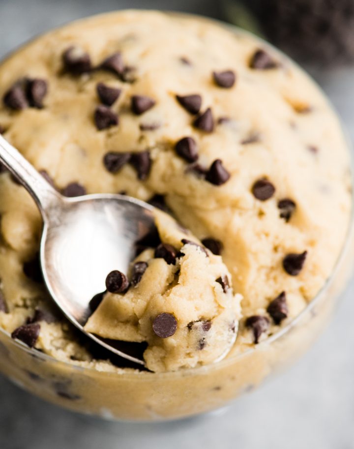 overhead photo of a spoon scooping a bite of edible cookie dough out of a glass dish