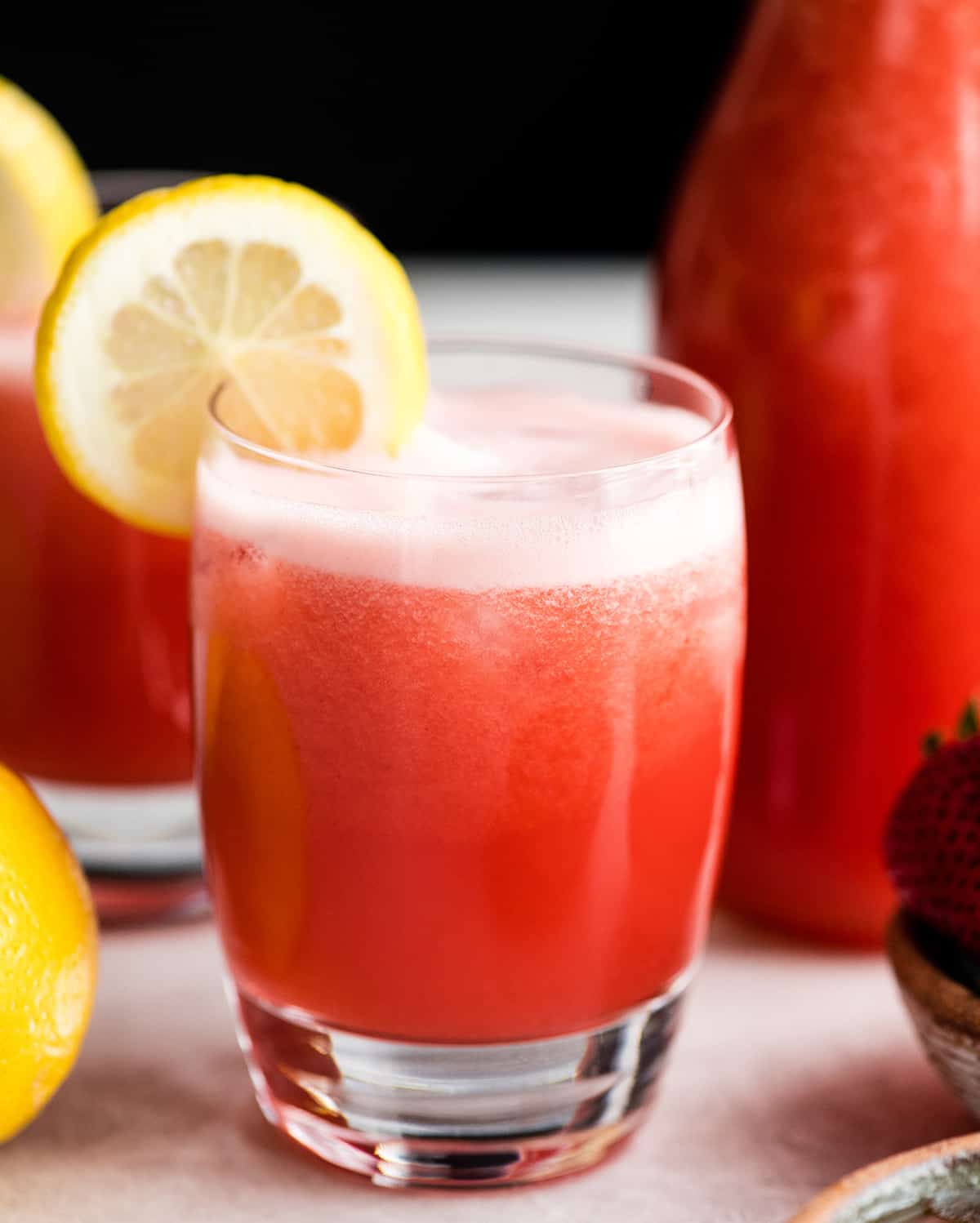 front view of a glass of Homemade Strawberry Lemonade with a lemon slice on the rim of the glass