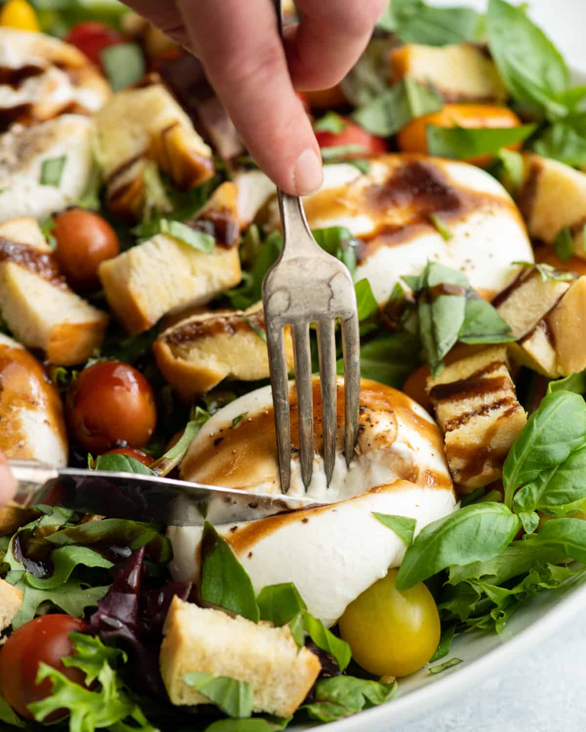 front view showing hands cutting open a piece of burrata cheese on a burrata salad