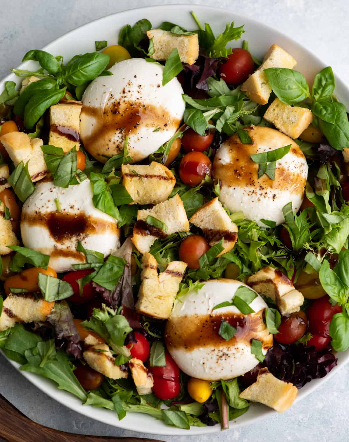 burrata salad in a large white serving dish drizzled with balsamic vinaigrette