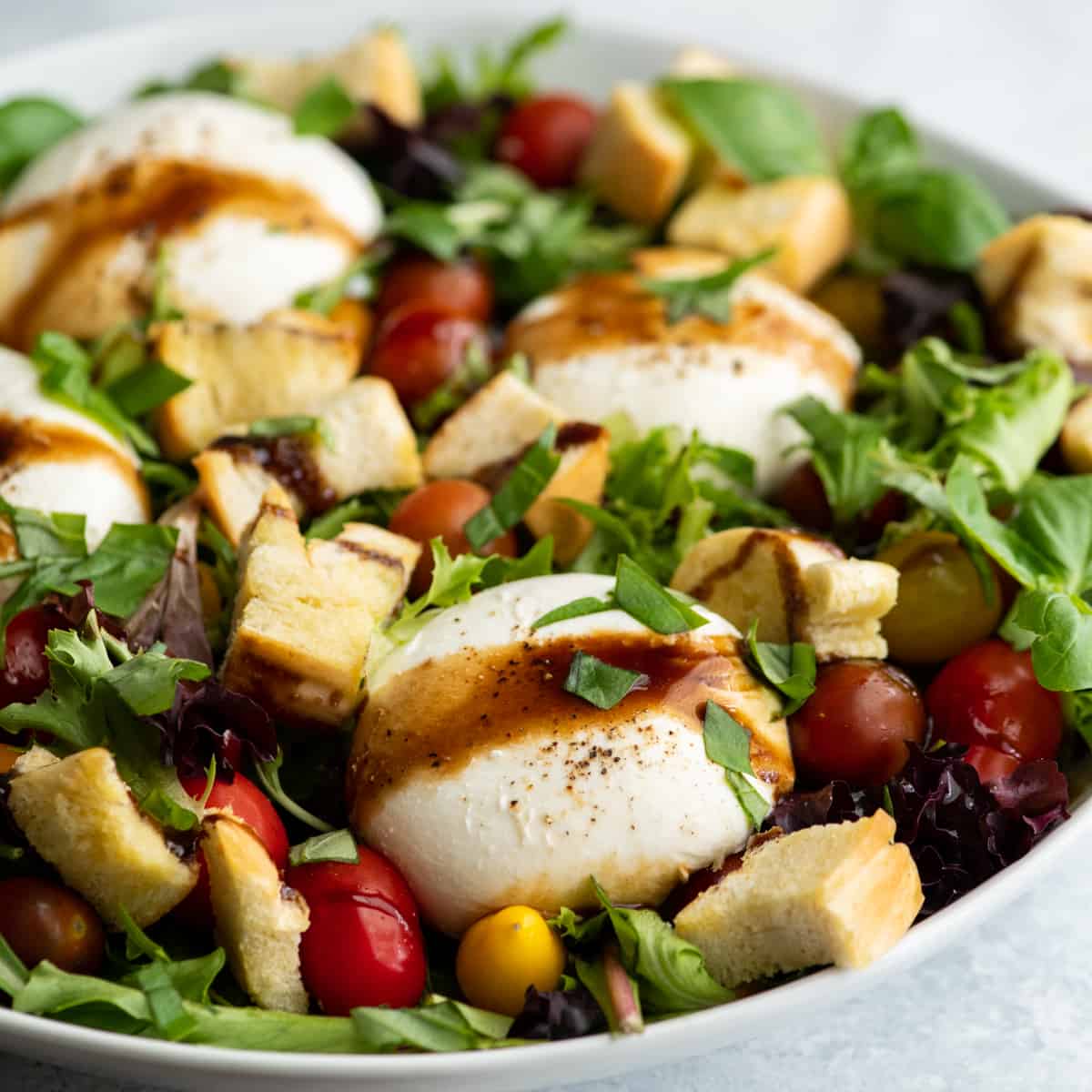 burrata salad in a large white serving dish drizzled with balsamic vinaigrette