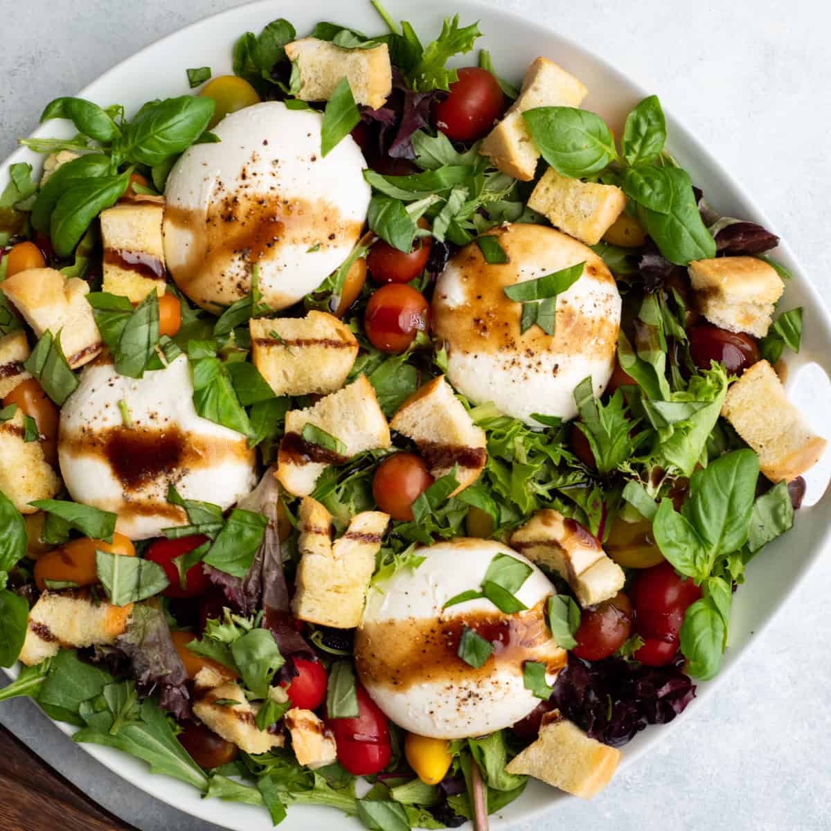 burrata salad in a large white serving dish drizzled with balsamic vinaigrette