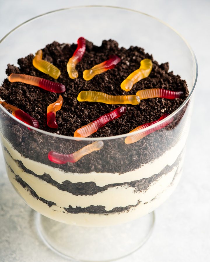 Front view of this Oreo Dirt Cake Recipe in a glass trifle dish with three layers of pudding and three layers of crushed Oreos with gummy worms on top