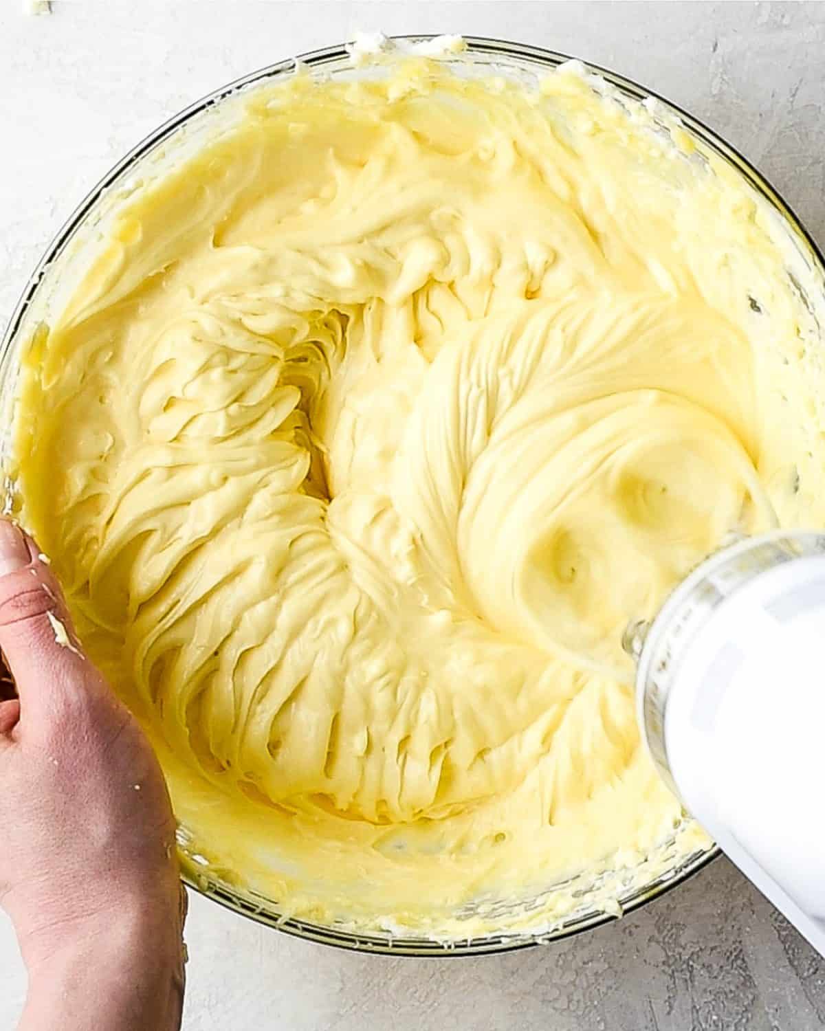 making oreo dirt cake recipe - filling being beat with a handheld mixer in a glass bowl on a gray surface 