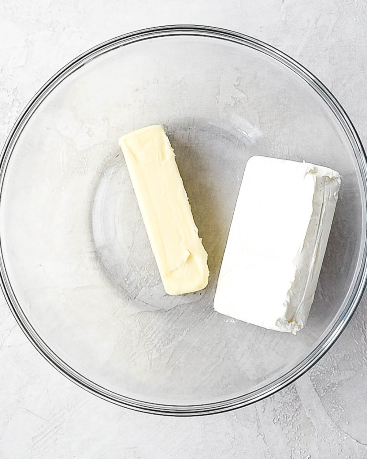 making oreo dirt cake recipe - a stick of butter and a block of cream cheese in a large glass bowl on a gray surface