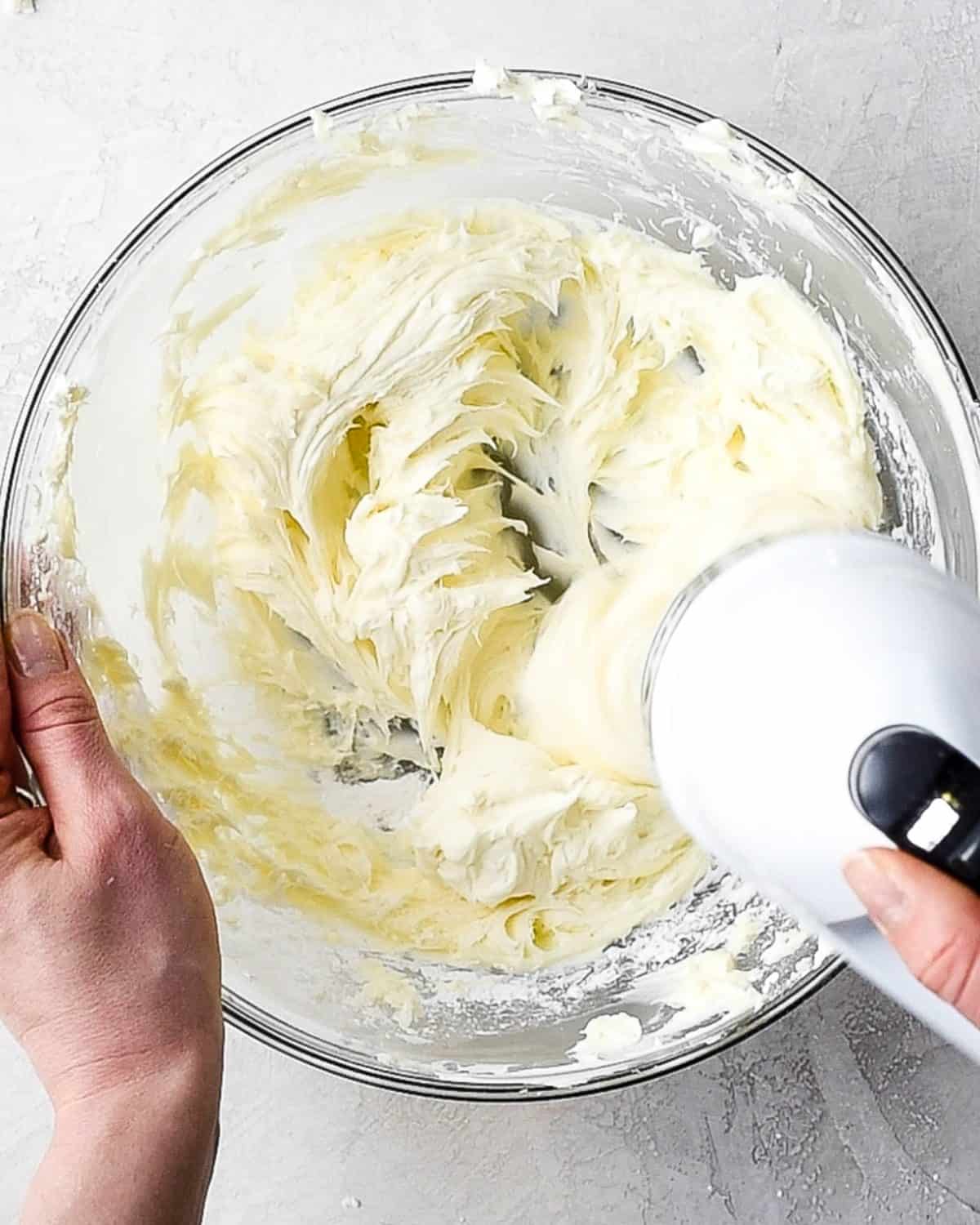 making oreo dirt cake recipe - hands beating powdered sugar into a large glass bowl with a white handheld mixer 