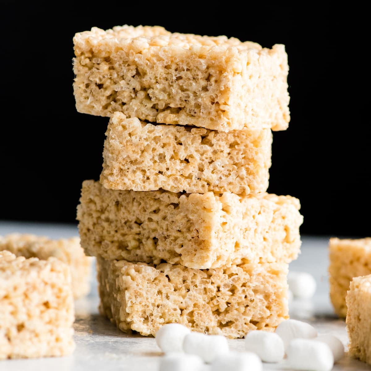 front view of a stack of 5 Rice Crispy Treats with four other rice crispy treats and mini marshmallows around it. 