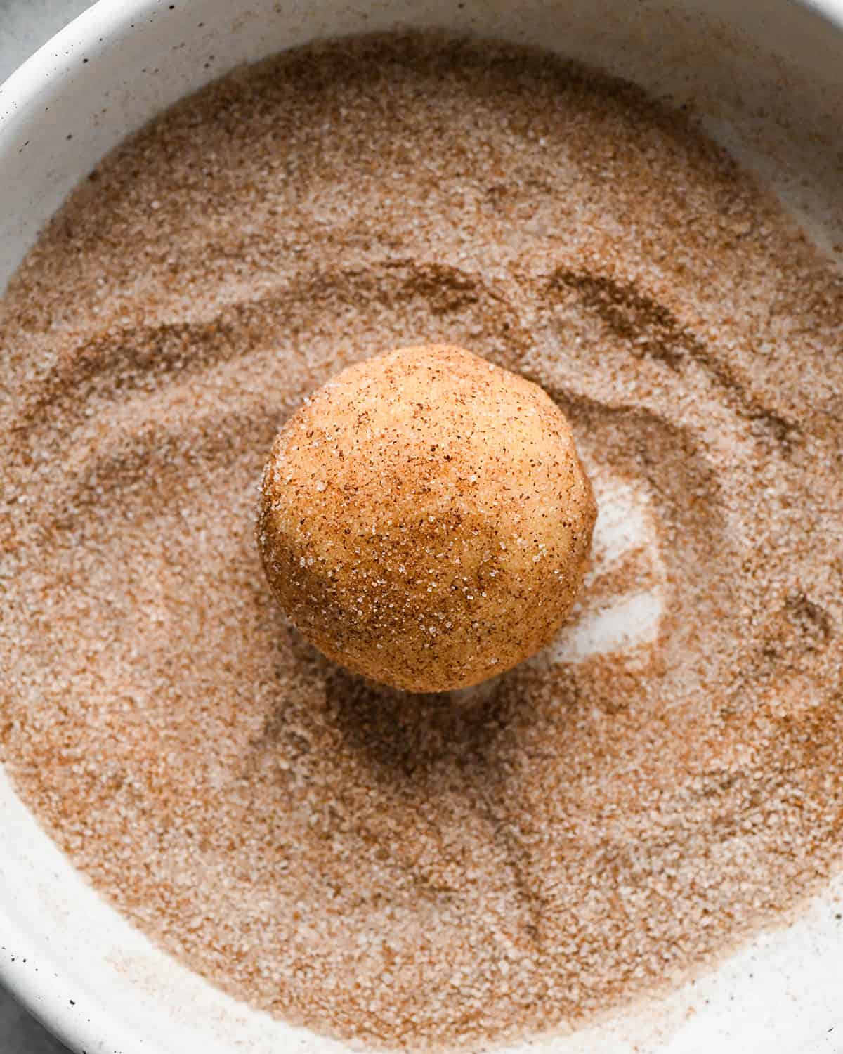 up close front view of a Snickerdoodle Cookie dough ball being rolled in cinnamon sugar