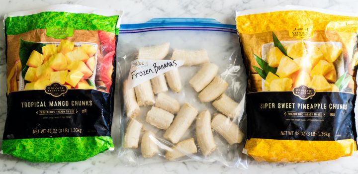 overhead view of two bags of frozen fruit (pineapple and mango) and a bag of frozen bananas cut in half ready to make this Green Smoothie Recipe