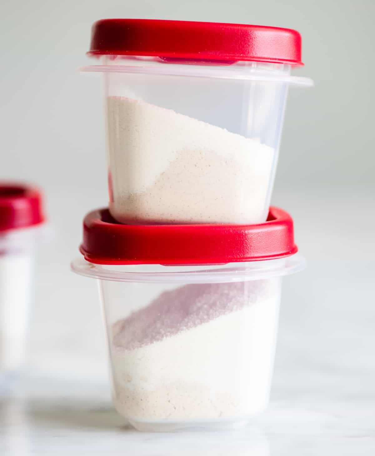 front view of two plastic containers with red lids stacked on each other with white protein powders inside to make this Green Smoothie Recipe